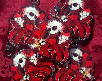 May include: Keychains featuring a red and black cartoon character with white hair, sunglasses, and a sword. The character is set against a red gear design. Each keychain has a silver clasp.