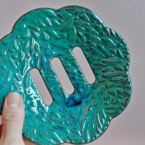 May include: A teal blue ceramic soap dish with a leaf pattern and three drainage holes.