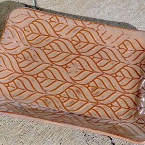 May include: A rectangular ceramic tray with a glossy finish, featuring a repeating embossed leaf pattern in shades of light brown and tan. The surface has a smooth, glazed texture with darker brown accents highlighting the intricate leaf veins.