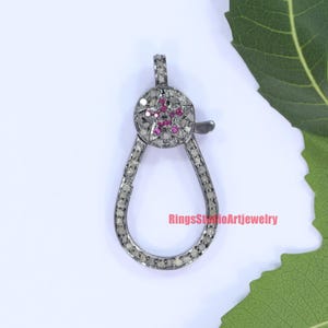 May include: A silver clasp with a star-shaped design set with small pink and white gemstones. The clasp is designed to be used as a connector for jewelry.
