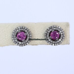 May include: A pair of silver stud earrings with a pink gemstone surrounded by a halo of small diamonds.