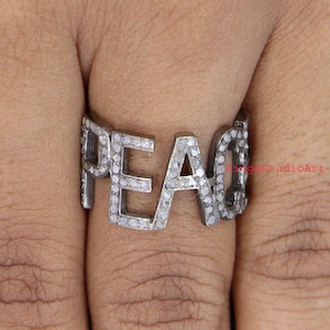 May include: A silver ring with the word "PEACE" spelled out in pave diamonds.