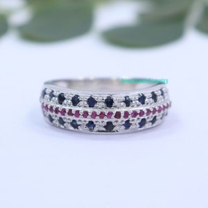 Może przedstawiać: Srebrny pierścionek z paskiem z rzędem czerwonych kamieni szlachetnych i dwoma rzędami niebieskich kamieni szlachetnych.