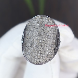 May include: A silver ring with a large oval-shaped centre stone set with many small diamonds. The ring has a textured band.