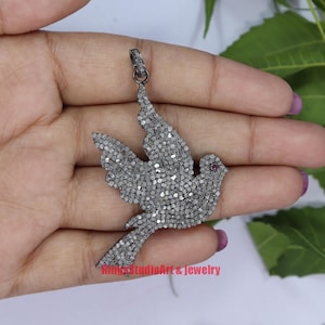 May include: Silver pendant featuring a dove with a red gemstone eye, covered in pave set white diamonds.