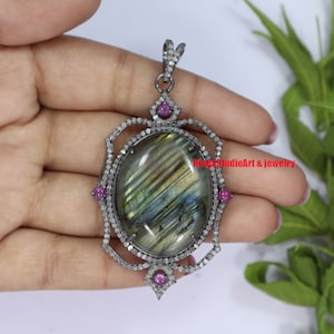 May include: A silver pendant with a large oval labradorite gemstone surrounded by a halo of small diamonds. The pendant is accented with four small pink gemstones.