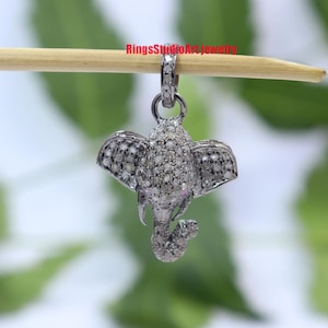 May include: A silver elephant pendant charm with a detailed design, covered in small white diamonds. The pendant is hanging from a wooden stick.