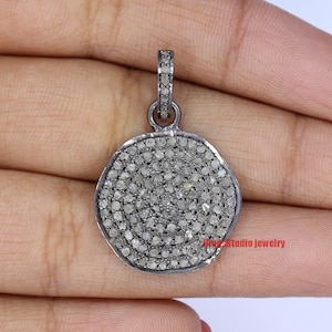 May include: A silver pendant with a round, pave-set diamond design. The pendant is approximately 1 inch in diameter and has a bail for attaching to a chain.