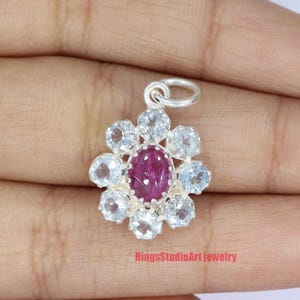 May include: A silver pendant featuring a pink gemstone surrounded by clear gemstones in a flower shape.