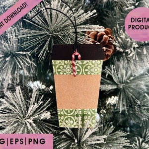 Puede incluir: Adorno navideño con forma de taza de café. Presenta un diseño de taza de papel marrón, una banda estampada verde y una parte superior negra. Un bastón de caramelo rojo y blanco cuelga de la parte superior. Las palabras "INSTANT DOWNLOAD!" y "DIGITAL PRODUCT" son visibles.