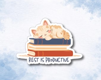 May include: A die-cut sticker featuring a light orange tabby kitten sleeping on a stack of three books. The books are colored dark blue, cream, and red. Below the books, the text REST IS PRODUCTIVE is printed in a dark gray, sans-serif font.