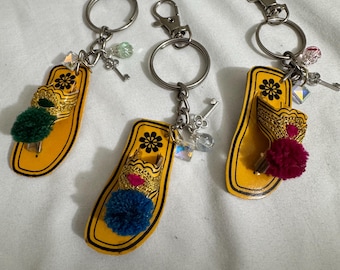 May include: Three yellow leather slipper keychains with silver key rings and charms. Each keychain has a small pom-pom and a decorative design.