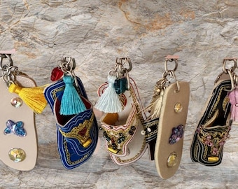 May include: Five colorful leather slipper keychains with beaded embellishments and tassels. The keychains are hanging from silver key rings.