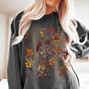 May include: Dark gray sweatshirt featuring a floral design with orange, yellow, and red flowers. The crew neck sweatshirt has long sleeves and a relaxed fit. The floral graphic is centered on the front of the shirt.