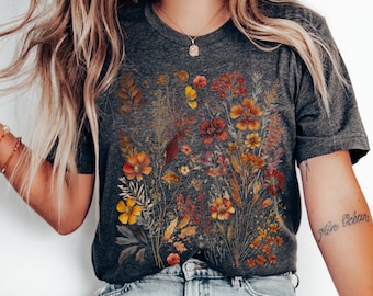 May include: A charcoal grey t-shirt with a floral print featuring dried flowers in shades of orange, yellow, and red. The flowers are arranged in a bouquet-like design.