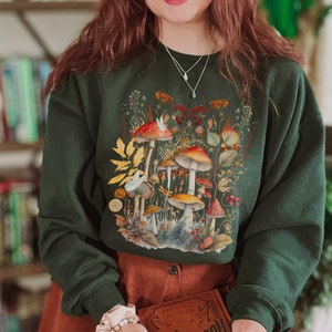 Pode incluir: Uma camisa de frio verde escura com uma ilustra&ccedil;&atilde;o colorida de cogumelos e o texto "Shroom Queens".