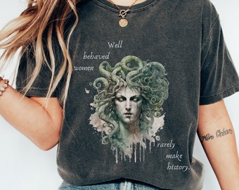 May include: Dark gray t-shirt featuring a Medusa graphic with green and white accents. The shirt has the text "Well behaved women rarely make history."