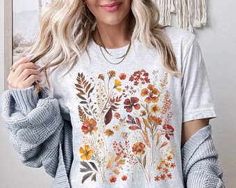 May include: A grey t-shirt with a floral print featuring a variety of orange, yellow, and brown flowers and leaves.