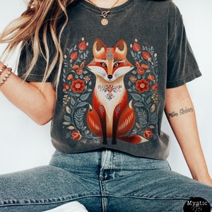 May include: Dark grey t-shirt with a fox illustration. The fox is in orange, red, and white, surrounded by red, yellow, and green floral designs. The shirt has a vintage, washed appearance.