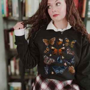 May include: Black sweatshirt with a colorful butterfly print. The butterflies are in various shades of brown, orange, blue, and black.