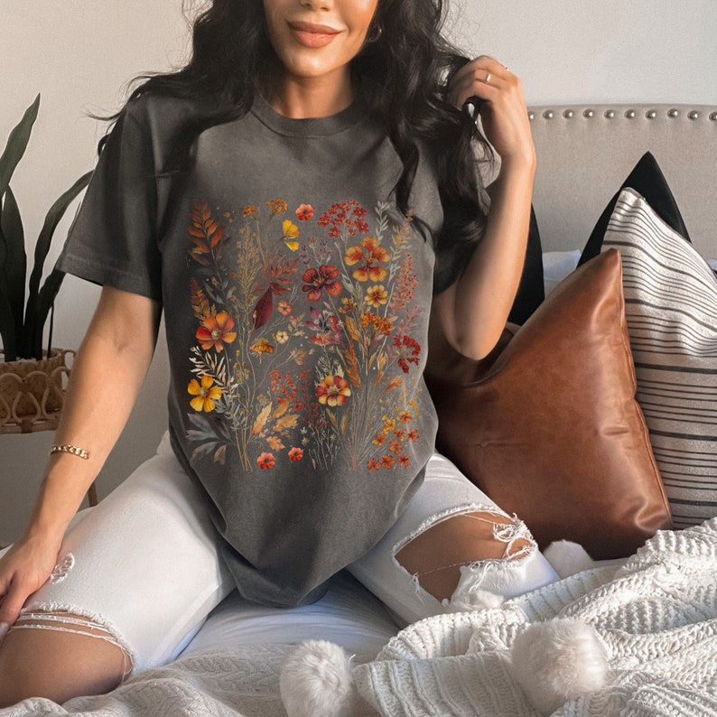 Op de afbeelding: Een grijs T-shirt met een bloemenprint met oranje, gele en rode bloemen. Het shirt heeft een losse pasvorm en een ronde hals.