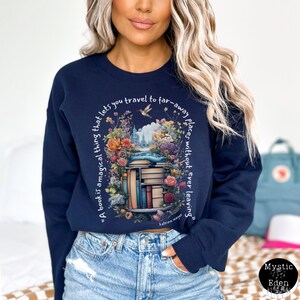 K&ouml;nnte beinhalten: Navyblauer Sweatshirt mit einem Aufdruck einer B&uuml;cherregals, das von Blumen umgeben ist, und einem Zitat, das lautet: "Ein Buch ist eine magische Sache, die es dir erm&ouml;glicht, an ferne Orte zu reisen, ohne jemals zu gehen".