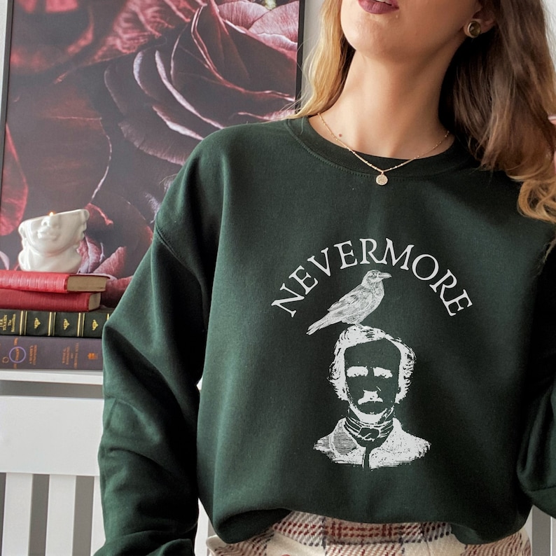 May include: A dark green sweatshirt with a white graphic print of Edgar Allan Poe with a raven perched on his head. The text "NEVERMORE" is printed above the graphic.