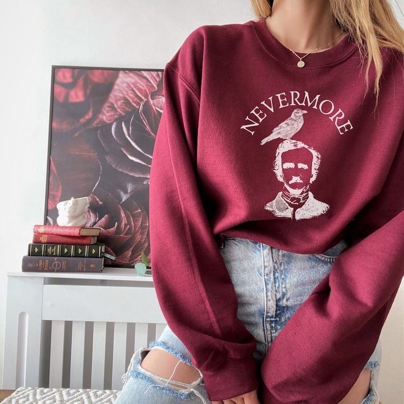 May include: A maroon sweatshirt with a white graphic print of a raven perched on the head of Edgar Allan Poe. The text "NEVERMORE" is printed in a circle around the image.