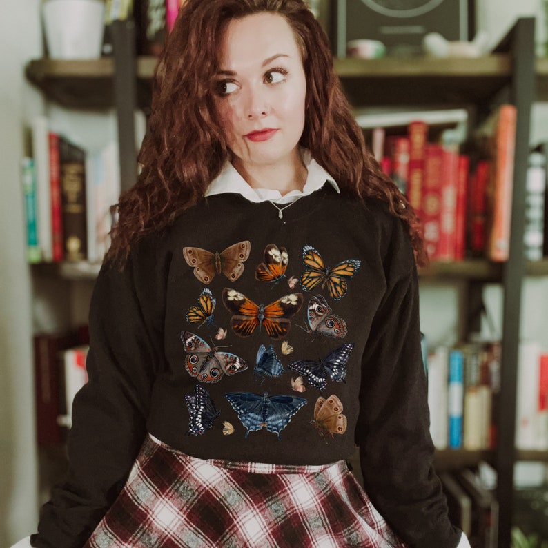 May include: A black cropped sweatshirt with a colorful butterfly print. The butterflies are arranged in a random pattern and are of various sizes and colors.
