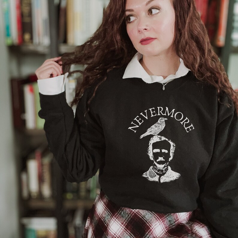 May include: A black sweatshirt with a white graphic of Edgar Allan Poe with a raven perched on his head. The text "NEVERMORE" is written in an arc above the graphic.