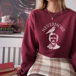 May include: A maroon sweatshirt with a white graphic print of Edgar Allan Poe with a raven perched on his head. The text "NEVERMORE" is printed around the image.