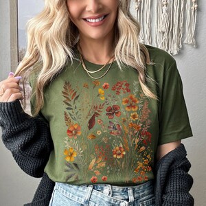 Puede incluir: Una camiseta verde con estampado floral con flores y hojas de color naranja, amarillo y marr&oacute;n.