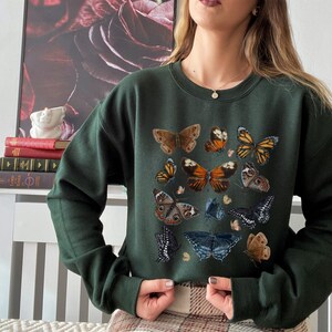 May include: A dark green sweatshirt with a print of various butterflies in shades of brown, orange, and black. The butterflies are arranged in a random pattern on the front of the sweatshirt.