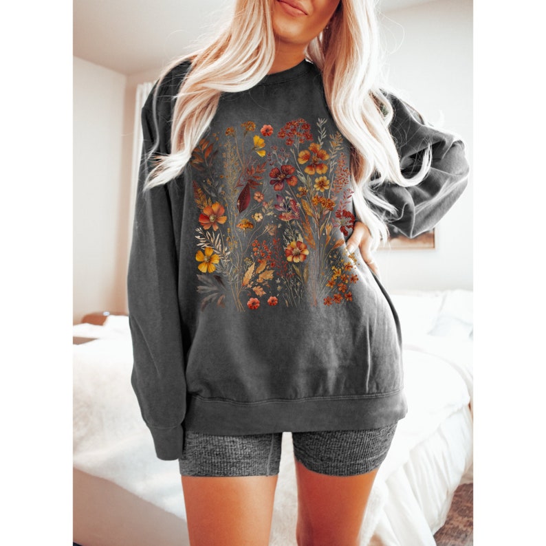 May include: Dark gray sweatshirt featuring a floral design with orange, yellow, and red flowers. The crew neck sweatshirt has long sleeves and a relaxed fit. The floral graphic is centered on the front of the shirt.