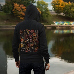 May include: Black zip-up hoodie with a floral print on the back. The print features a variety of flowers in shades of orange, yellow, and red.