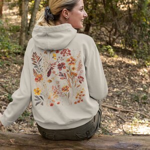 May include: A light gray hoodie with a floral print on the back. The print features a variety of flowers and leaves in shades of orange, yellow, and red.