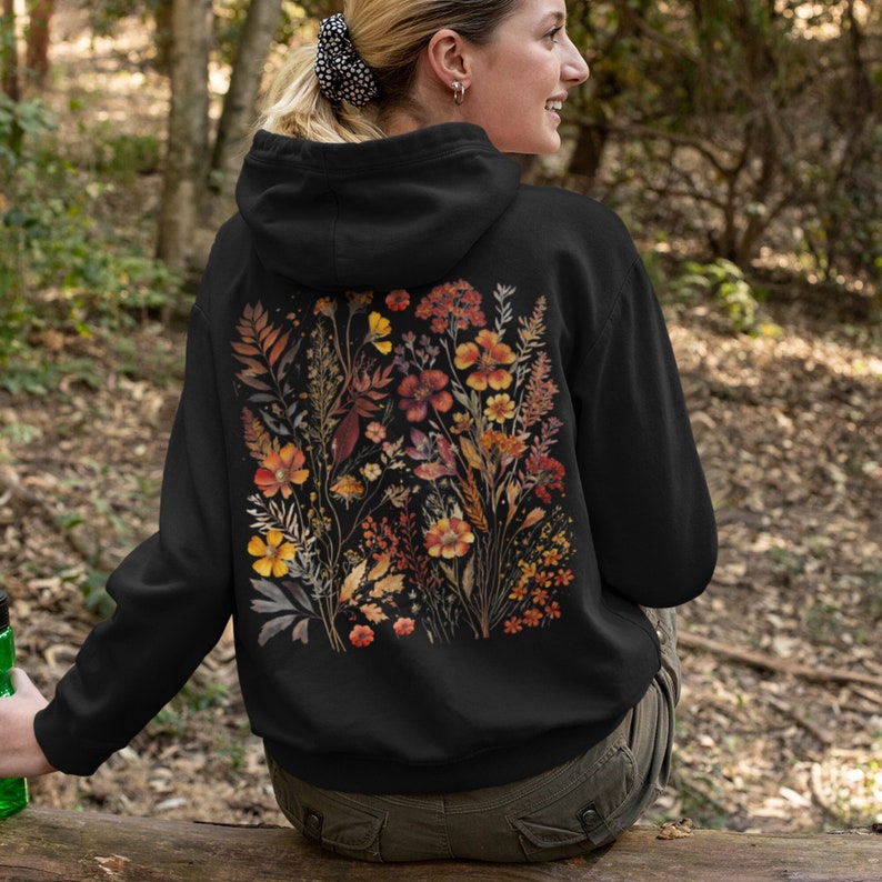 May include: Black hoodie with a floral print on the back. The print features a variety of flowers and leaves in shades of orange, yellow, and brown.