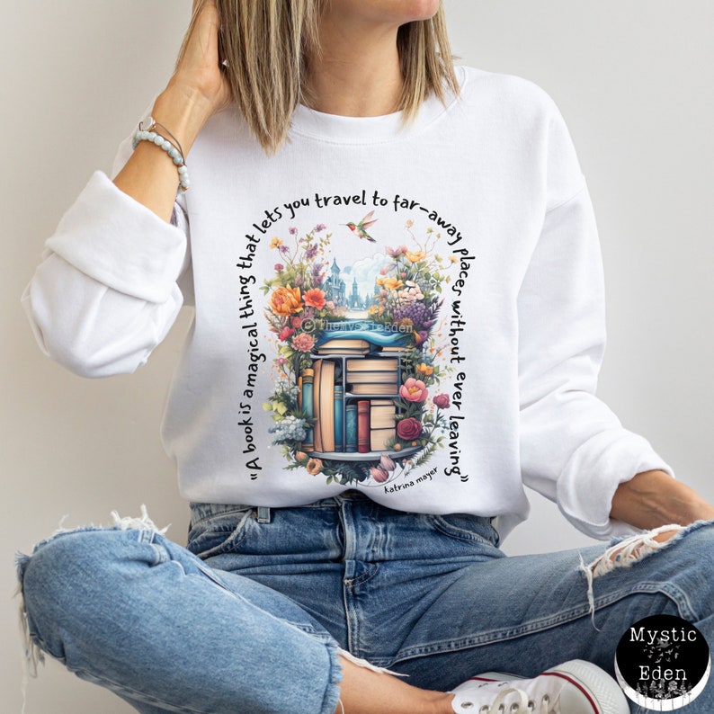 K&ouml;nnte beinhalten: Wei&szlig;es Sweatshirt mit einer bunten Grafik eines B&uuml;cherregals mit B&uuml;chern und Blumen. Der Text "Ein Buch ist eine magische Sache, die es dir erm&ouml;glicht, an ferne Orte zu reisen, ohne jemals zu gehen" ist auf dem Sweatshirt gedruckt.