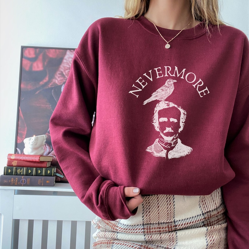 May include: A maroon sweatshirt with a white graphic print of Edgar Allan Poe with a raven on his head. The text "NEVERMORE" is printed around the graphic.