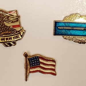Op de afbeelding: Drie gouden speldjes met patriottische thema's. De eerste speld heeft een adelaar die over een Amerikaanse vlag vliegt met de tekst "The Right to Keep and Bear Arms". De tweede speld heeft een blauw lint met een gouden geweer en een gouden krans. De derde speld heeft een kleine Amerikaanse vlag.