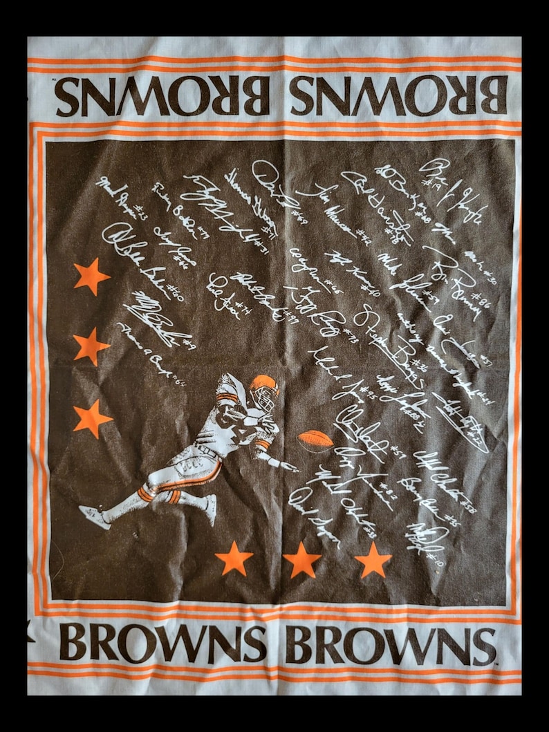 Puede incluir: Toalla del equipo de f&uacute;tbol americano Browns en marr&oacute;n y blanco con detalles en naranja. Presenta un gr&aacute;fico de un jugador de f&uacute;tbol, estrellas naranjas y firmas de jugadores. Las palabras "BROWNS" est&aacute;n impresas arriba y abajo.