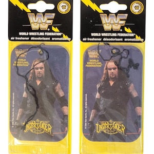 May include: Two air fresheners featuring The Undertaker from the World Wrestling Federation. Each air freshener is in a yellow package with the WWF logo and the text "air freshener désodorisant aromatizante". The Undertaker is depicted in a black outfit.