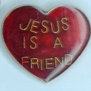 May include: Red heart-shaped pin with gold lettering that reads "JESUS IS A FRIEND".