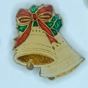 May include: Two gold-colored bells with a red and green holly and bow design. The bells are decorated with a gold glitter finish.