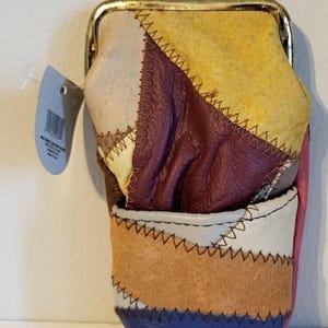 May include: A colorful patchwork leather coin purse with a gold-toned clasp. The purse features a variety of colors, including yellow, purple, white, brown, pink, and blue. The edges are stitched with black thread. A blue tag hangs from the side.