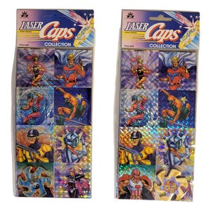 Può includere: Due confezioni di figurine della collezione Laser Caps. Ogni confezione presenta una varietà di immagini colorate a tema supereroi. La confezione include il testo "Laser Caps" e "Collection". Le carte hanno uno sfondo olografico e iridescente.