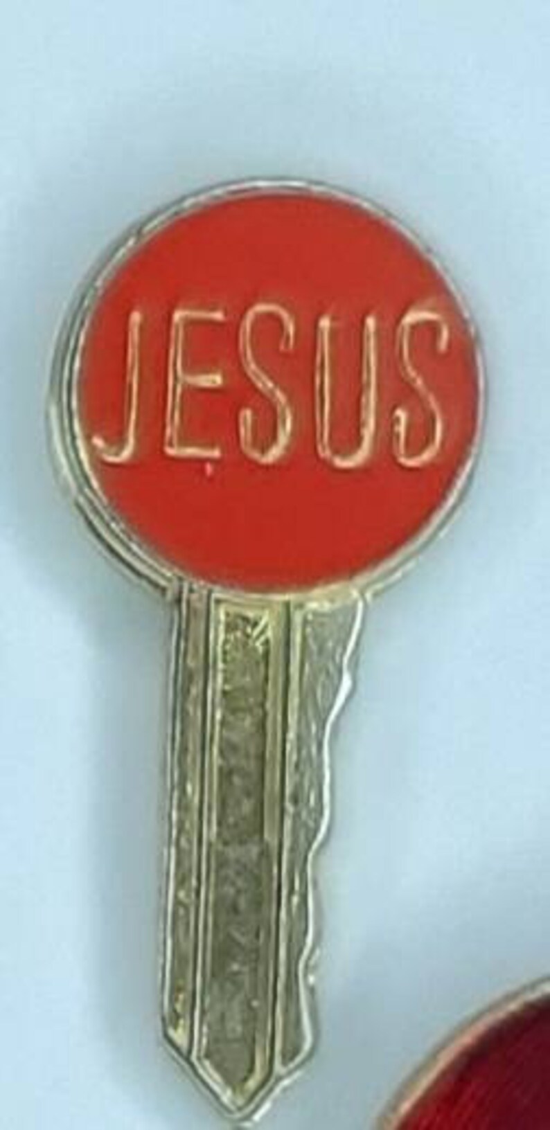 May include: A red key-shaped pin with the word "JESUS" in gold lettering.