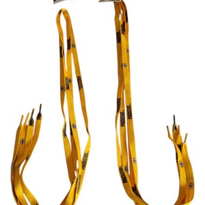 May include: Two pairs of yellow and green Packers-themed shoelaces with the team name printed on them. Each lace has a metal tip and a small NFL tag. The laces are displayed against a white background.