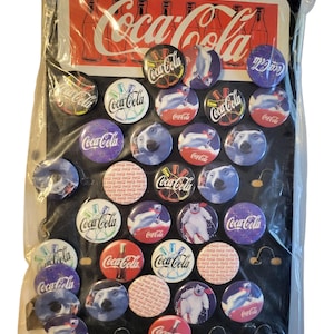 May include: A collection of Coca-Cola pins in a plastic package. The pins feature the Coca-Cola logo, polar bears, and other designs. The background includes a Coca-Cola advertisement with red and white colors.
