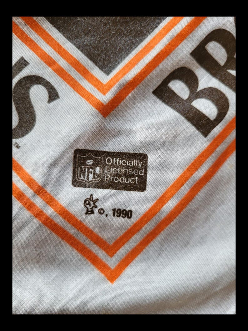 Puede incluir: Tela blanca con dise&ntilde;o geom&eacute;trico marr&oacute;n y naranja. La tela tiene las letras "BR" y "S" en marr&oacute;n. Se ve un logotipo de la NFL "Producto con licencia oficial", junto con el a&ntilde;o 1990.